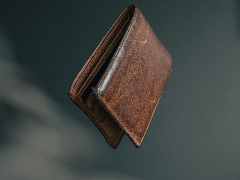 A slim leather wallet with credit cards on a dark surface, lit editorially