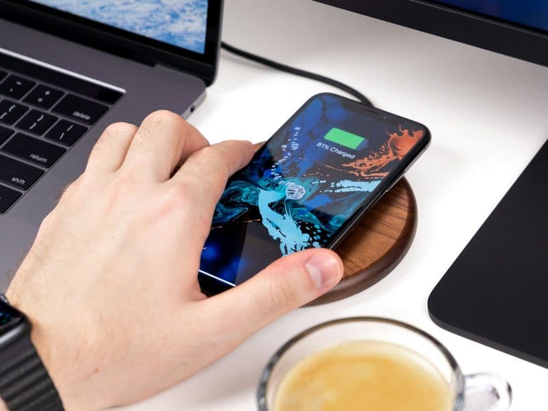 An iPhone charging wirelessly on a desk in front of a monitor