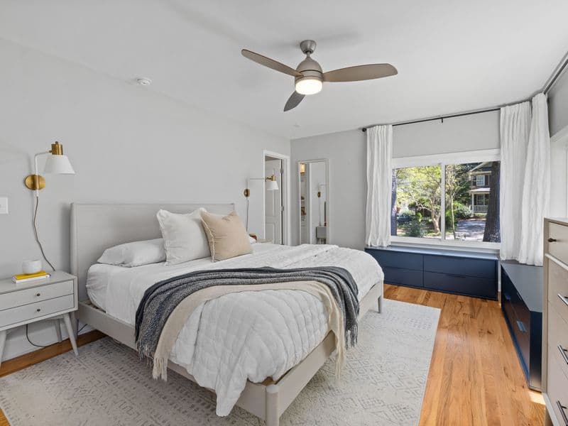 Bright, airy minimalist bedroom interior with a standing fan, evoking quiet summer cooling