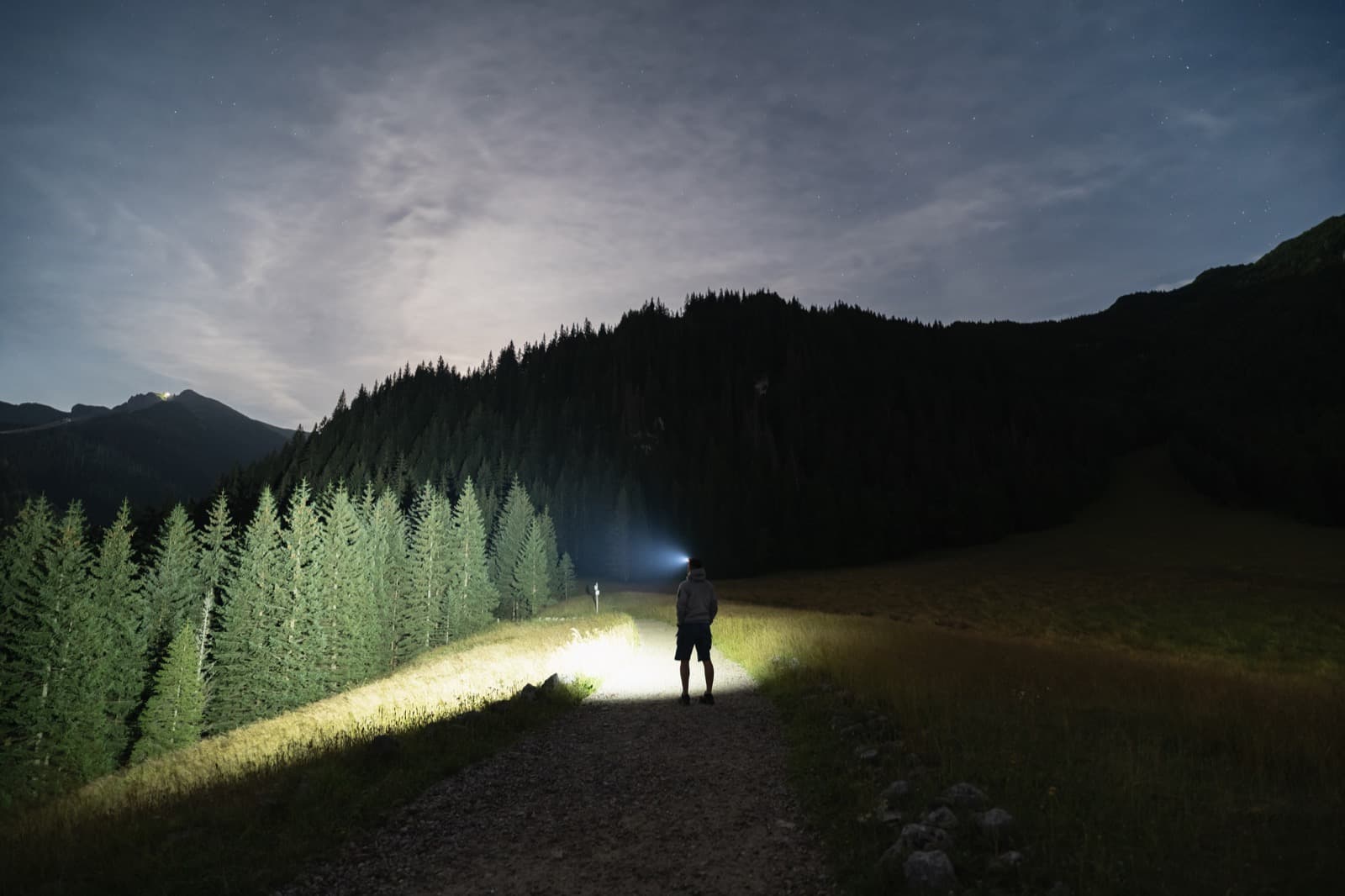 Hiker on a mountain trail at night with a rechargeable headlamp casting a beam of light down the path